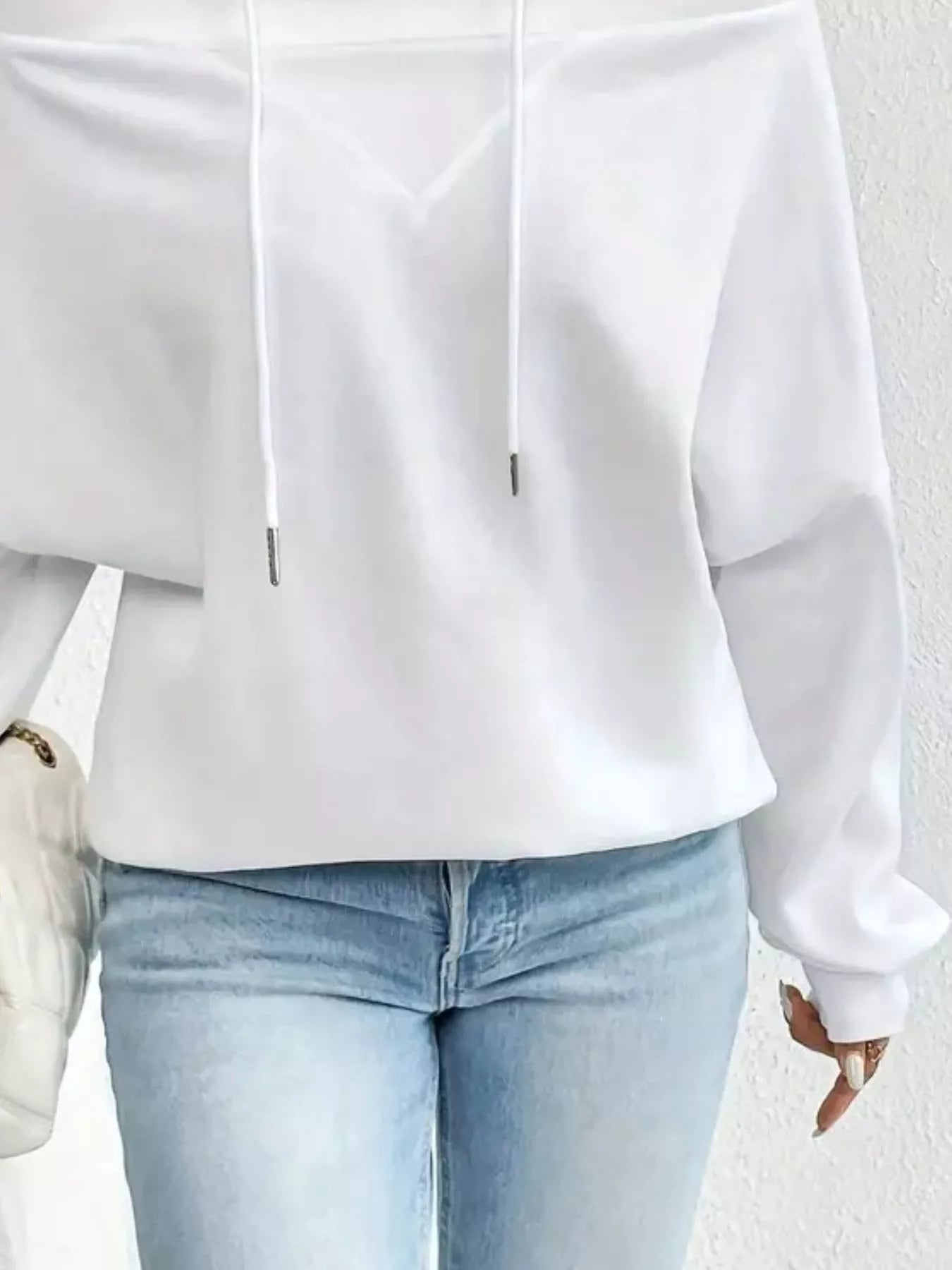 White blouse with long sleeves and light blue jeans on a neutral background