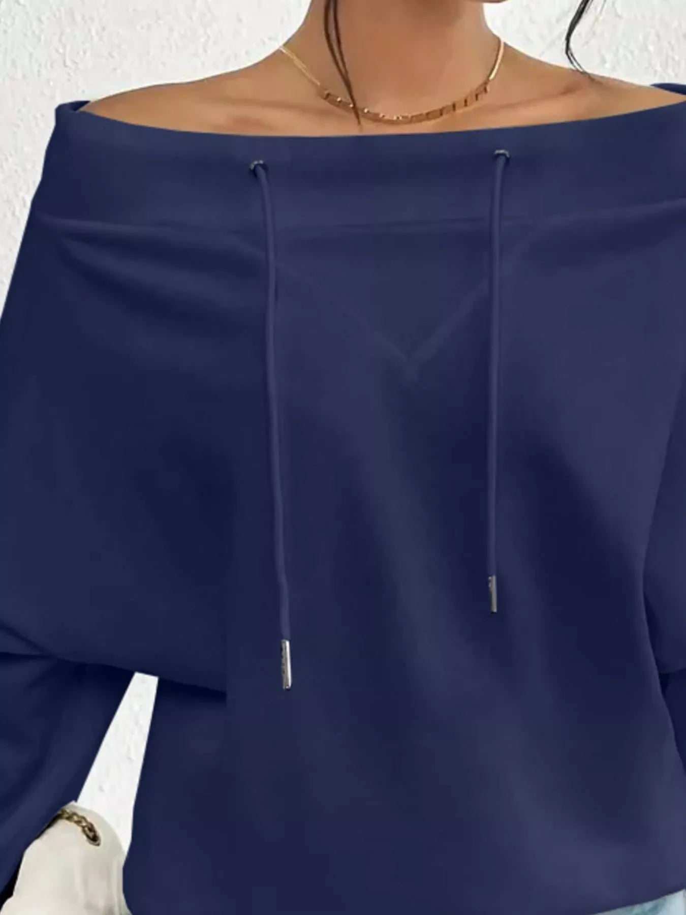 Navy blue off-shoulder top worn by a person with a white background