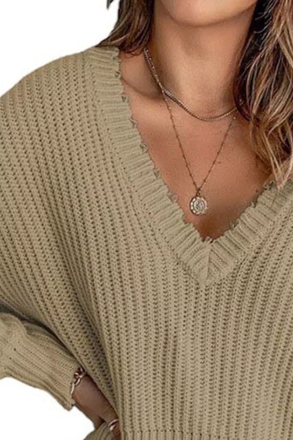 Woman wearing a khaki ribbed V-neck sweater with distressed raw hem and blue jeans.