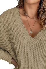 Woman wearing a khaki ribbed V-neck sweater with distressed raw hem and blue jeans.