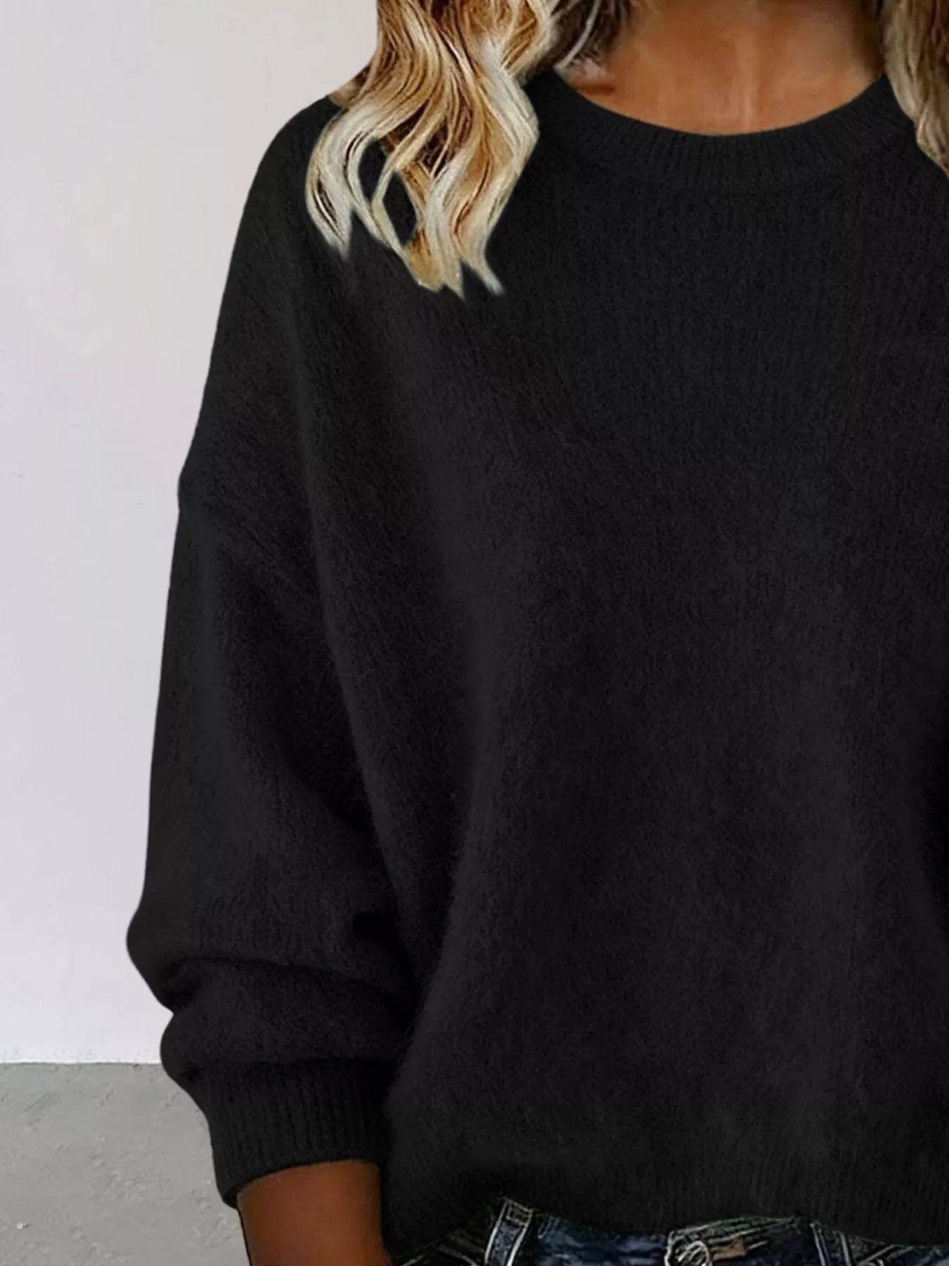 Woman wearing a black round neck dropped shoulder sweater with dark-wash jeans.