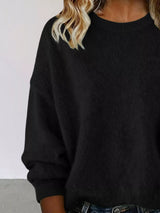 Woman wearing a black round neck dropped shoulder sweater with dark-wash jeans.