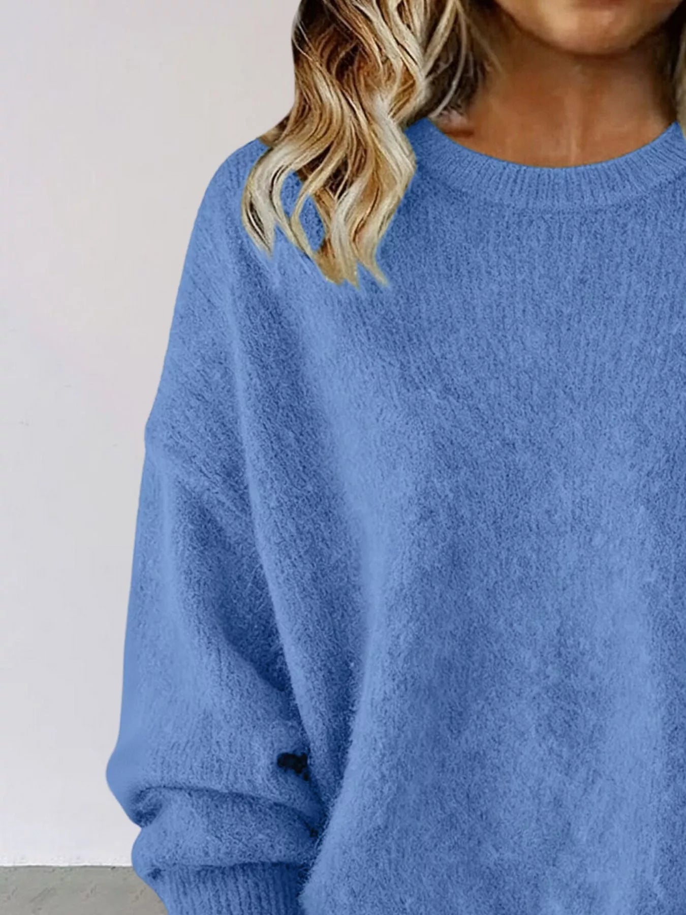 Woman wearing a blue round neck dropped shoulder sweater with dark-wash jeans.