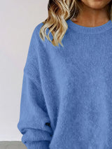 Woman wearing a blue round neck dropped shoulder sweater with dark-wash jeans.
