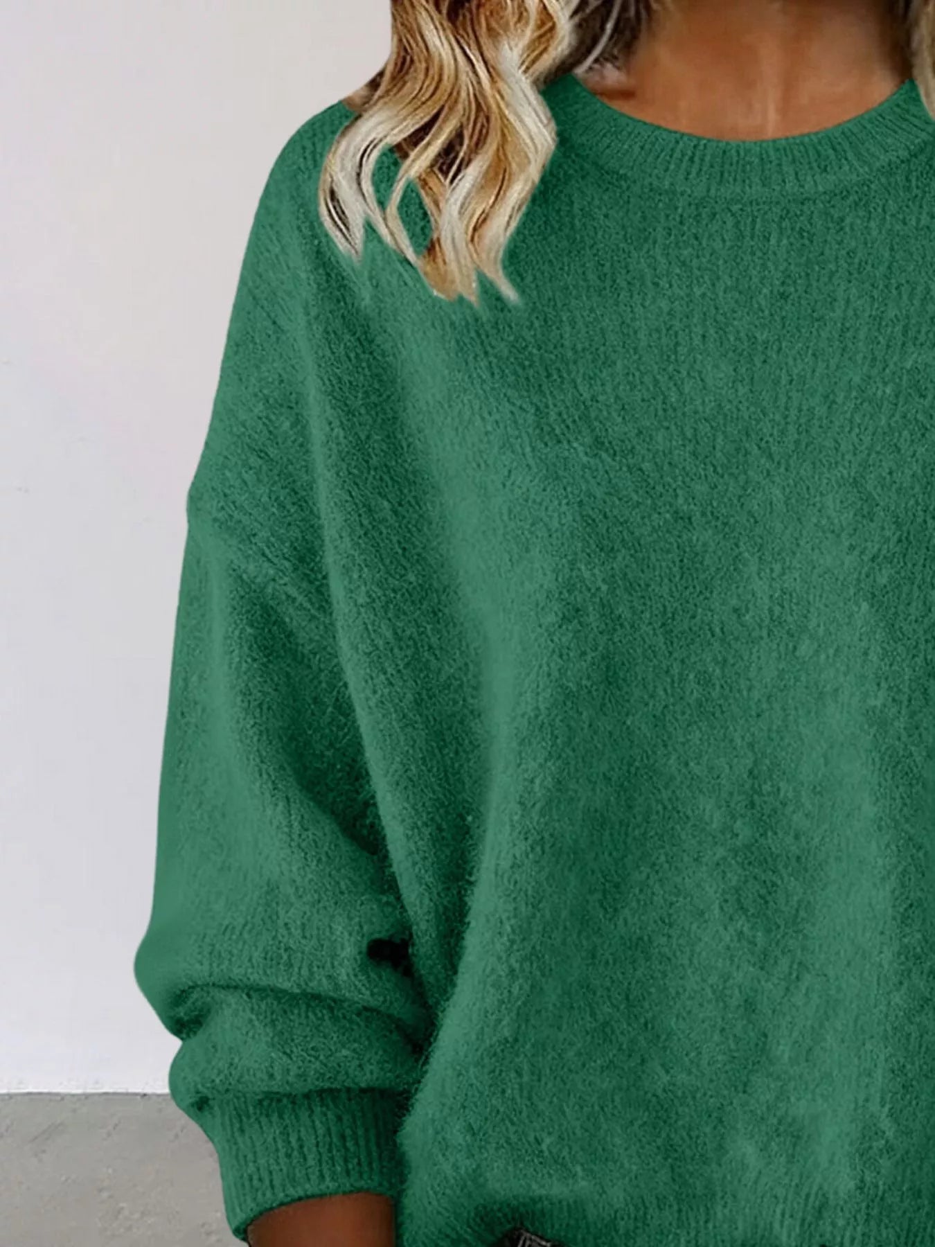 Woman wearing a green round neck dropped shoulder sweater with dark-wash jeans.