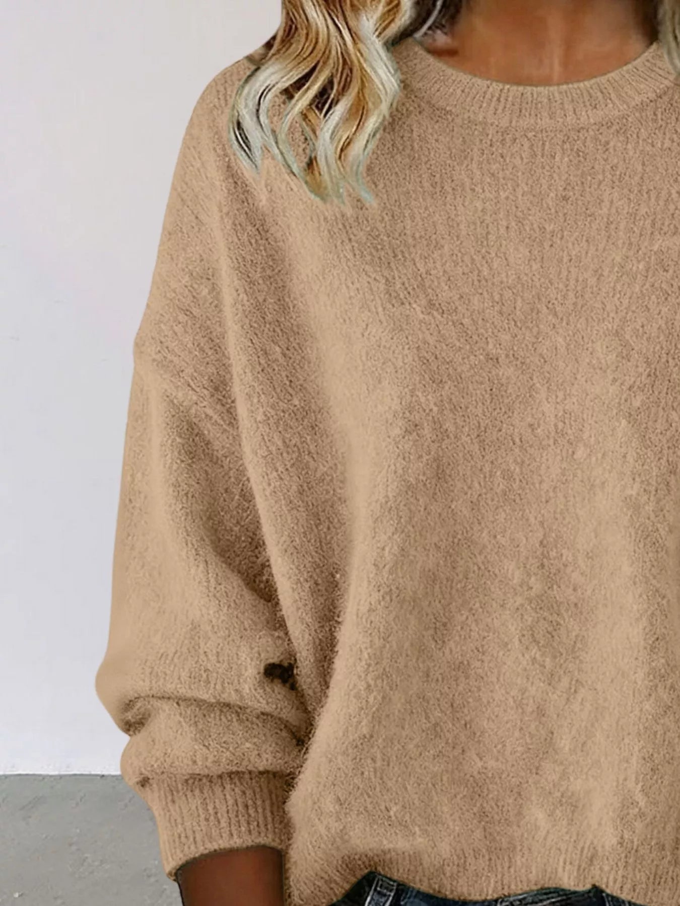 Woman wearing a Khaki round neck dropped shoulder sweater with dark-wash jeans.