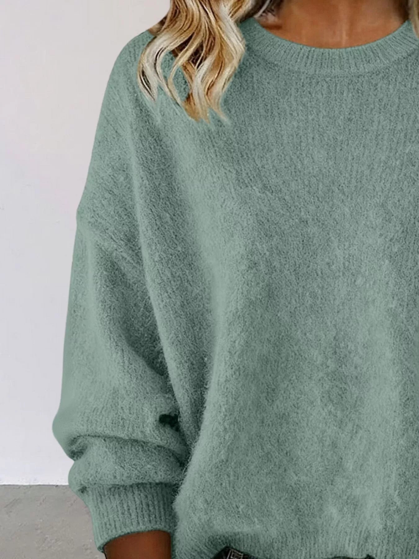 Woman wearing a light green round neck dropped shoulder sweater with dark-wash jeans.