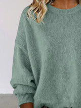 Woman wearing a light green round neck dropped shoulder sweater with dark-wash jeans.