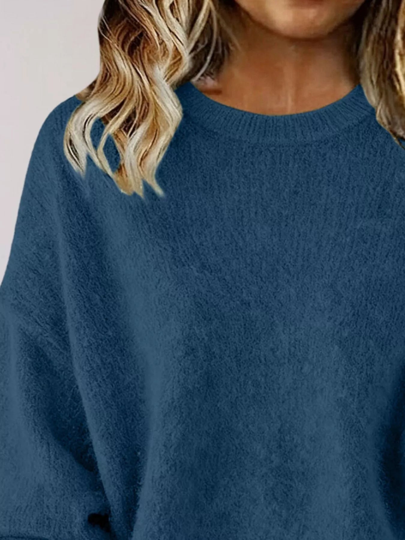 Woman wearing a navy-blue round neck dropped shoulder sweater with dark-wash jeans.