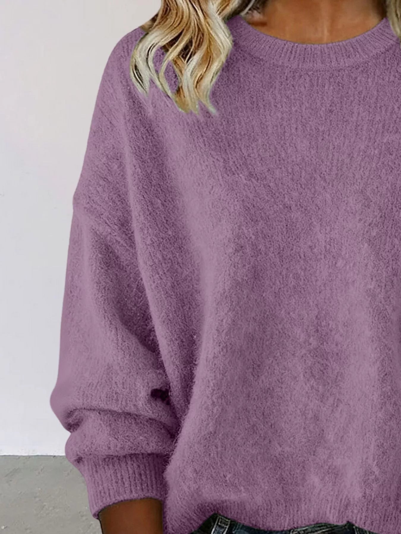 Woman wearing a purple round neck dropped shoulder sweater with dark-wash jeans.