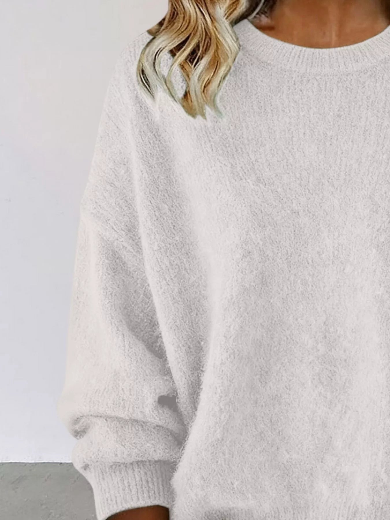 Woman wearing a white round neck dropped shoulder sweater with dark-wash jeans.