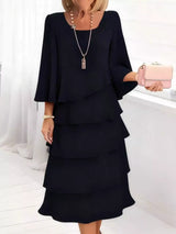 Woman wearing a black layered dress holding a pink clutch against a white background