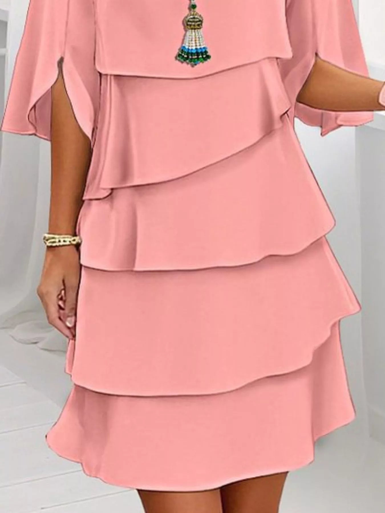 Coral layered dress with a decorative pendant on a white background