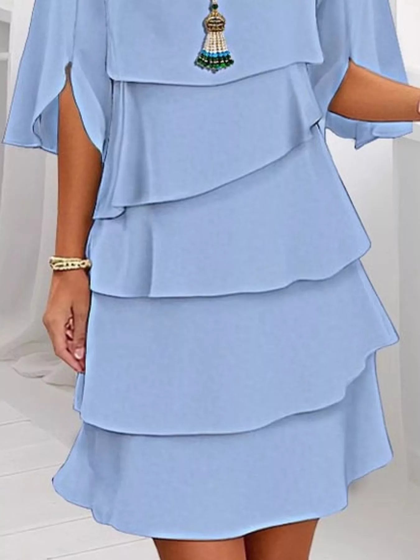 Light blue layered dress with a decorative brooch on a white background