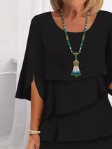 Person wearing a black layered top with a colorful beaded necklace against a white background