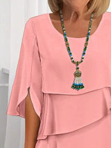 Person wearing a coral layered dress with a colorful beaded necklace.