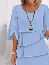 Woman wearing a light blue layered dress with a necklace against a white background