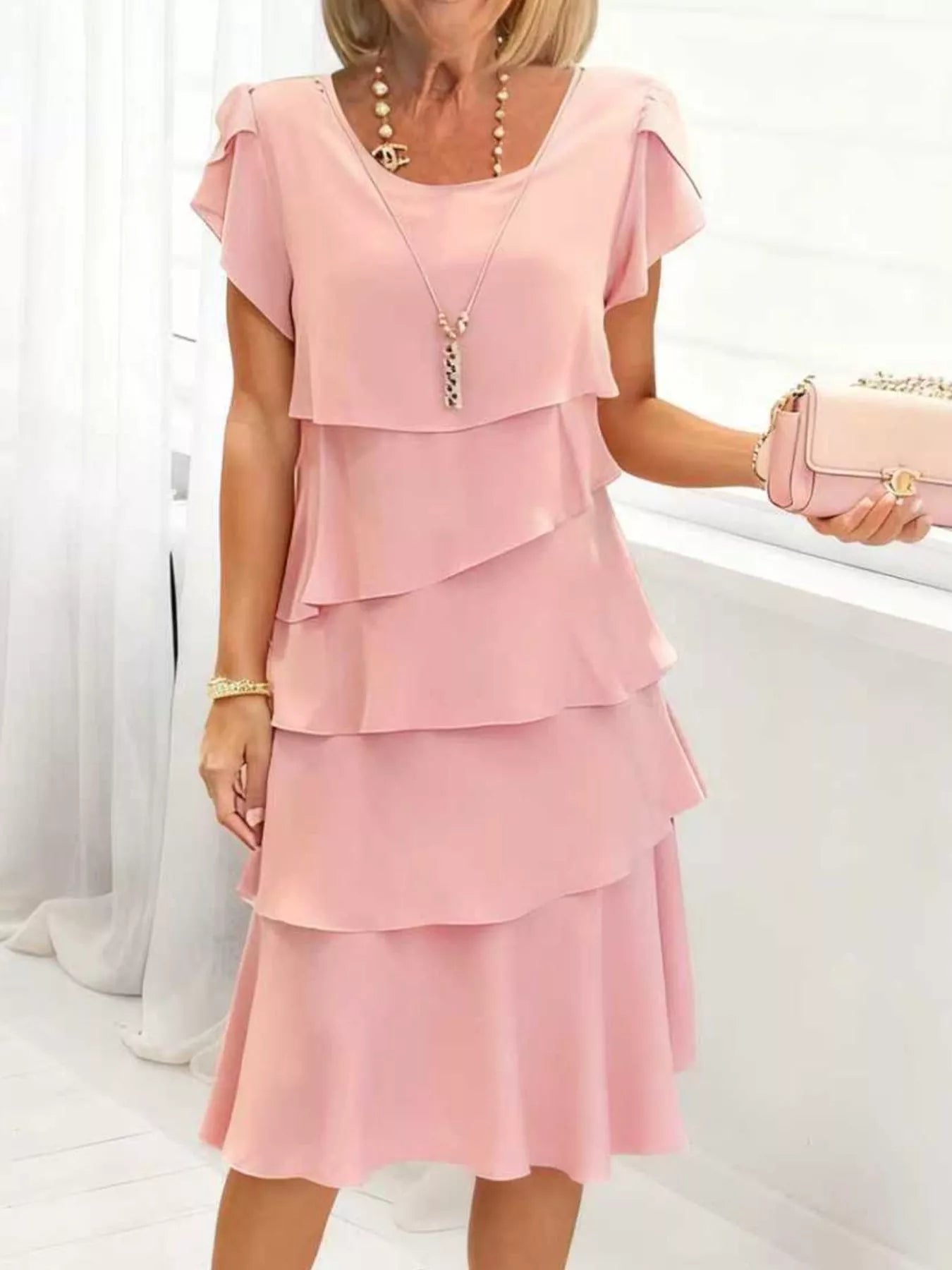 Woman wearing a blush pink layered dress with a white background