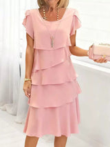 Woman wearing a blush pink layered dress with a white background