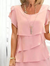 Woman wearing a blush pink layered dress with a necklace against a white background