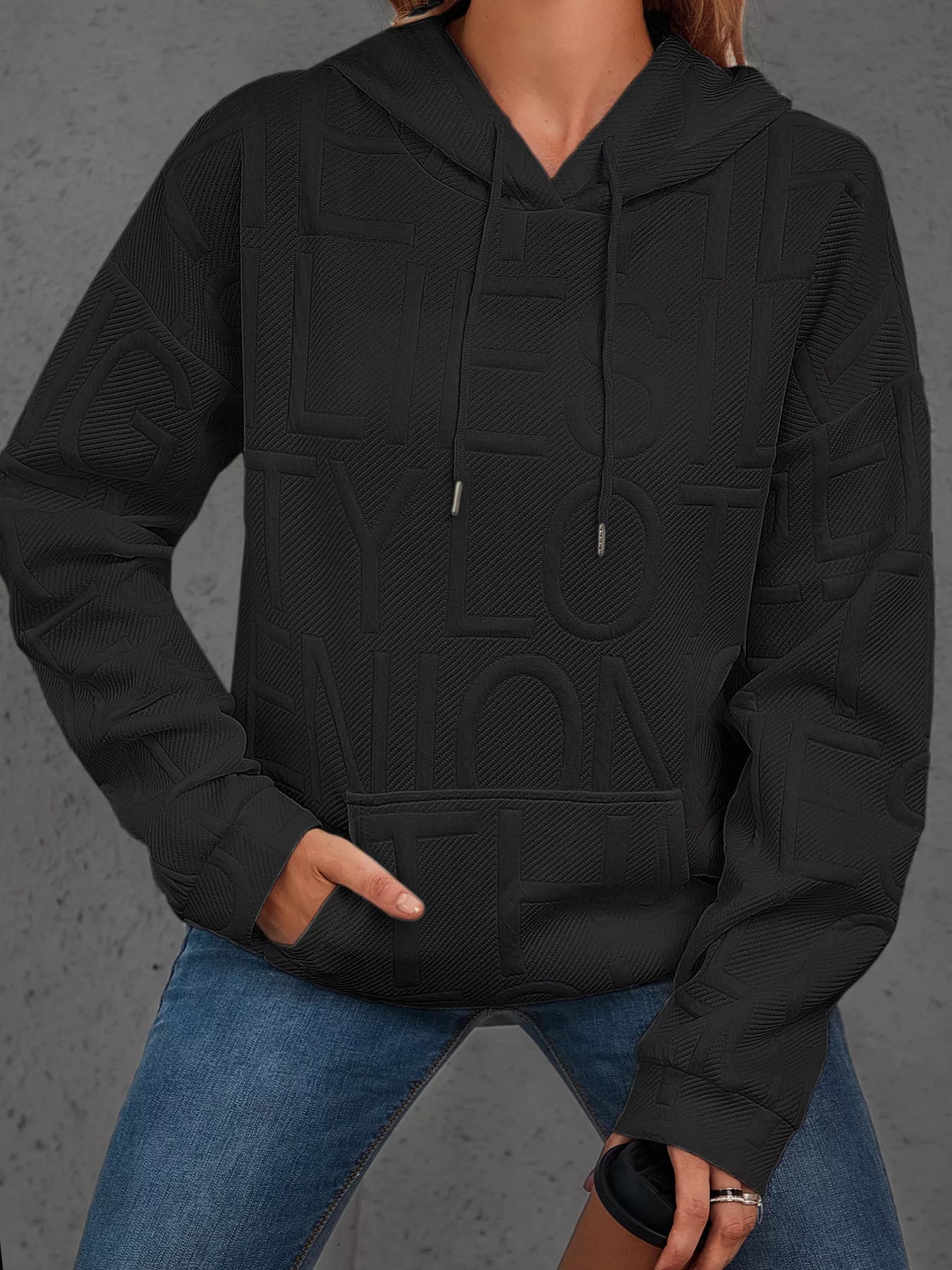 Person wearing a black hoodie with a textured pattern on a gray background