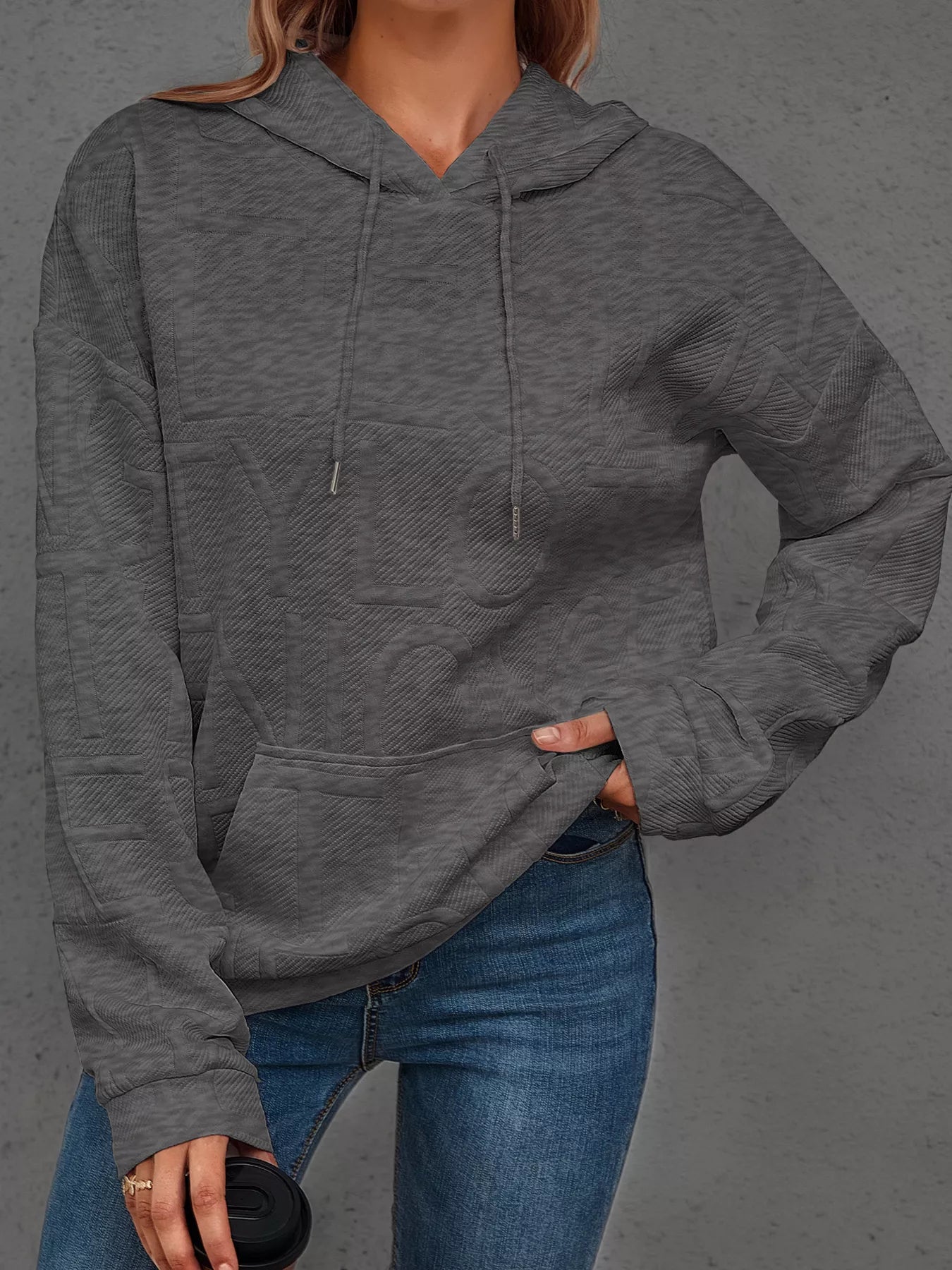 Person wearing a gray hoodie and blue jeans against a gray background