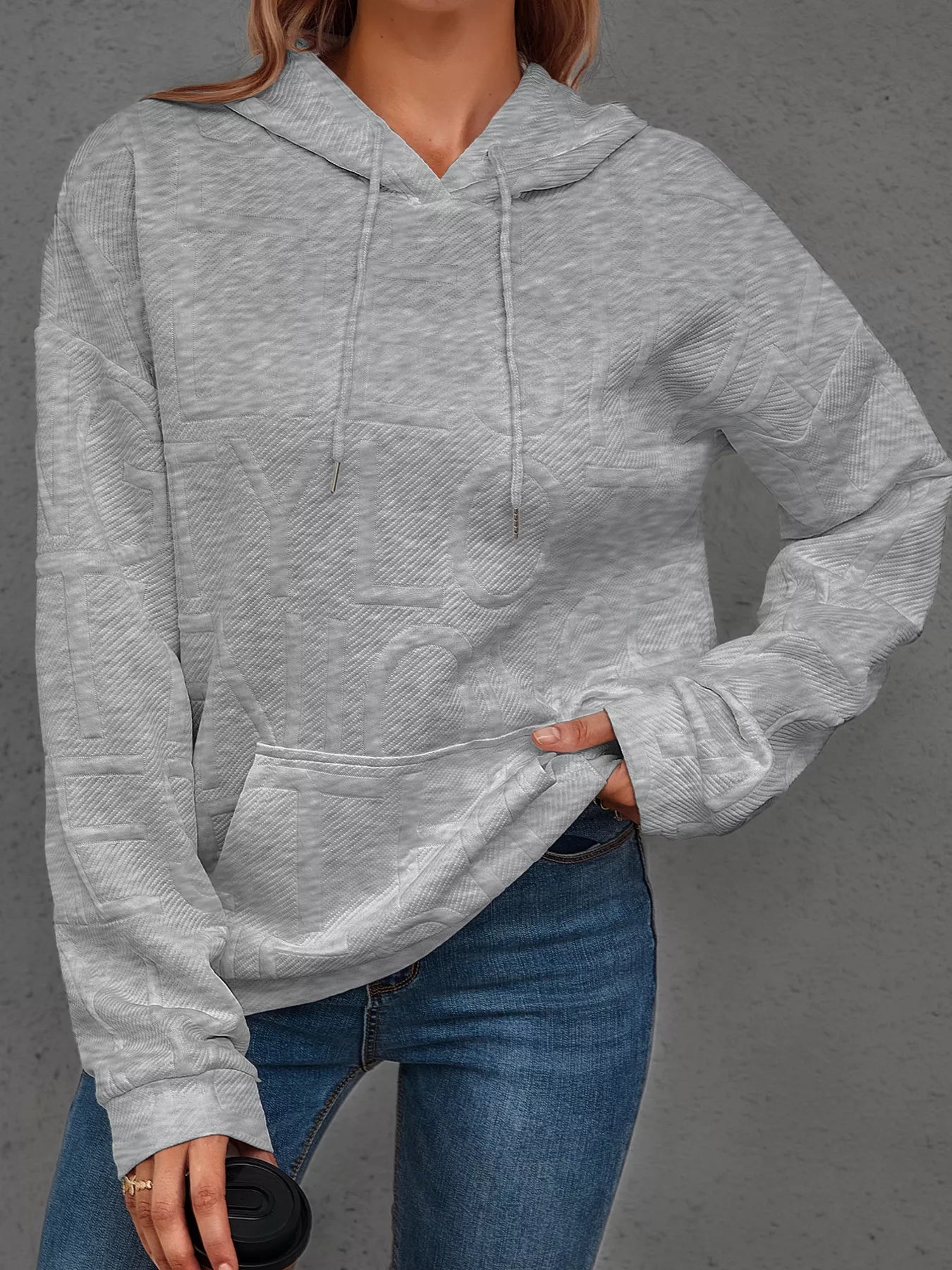 Person wearing a gray hoodie and blue jeans on a gray background