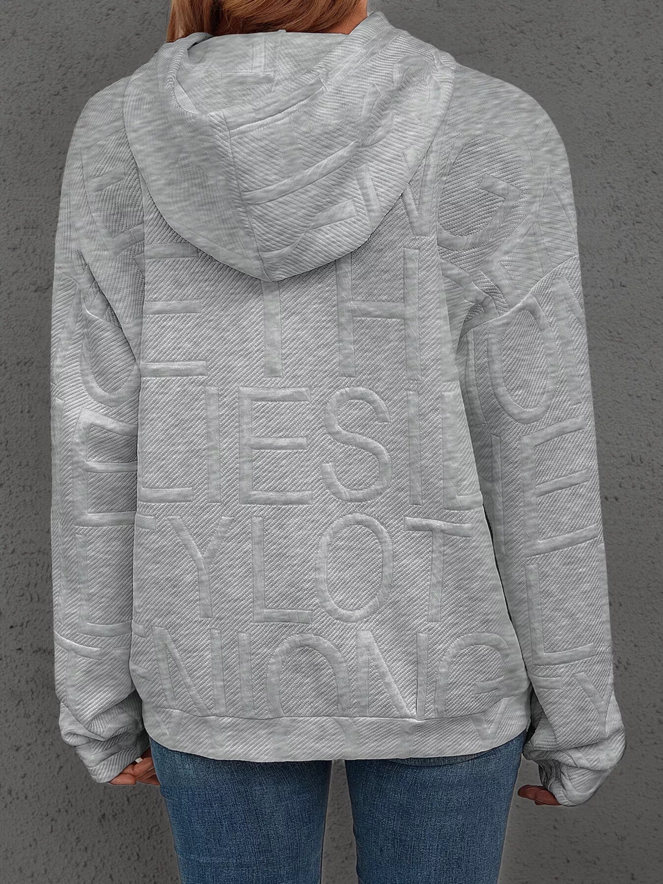Person wearing a gray hoodie with text on the back against a gray background