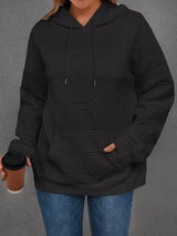 Person wearing a black hoodie holding a coffee cup against a gray background