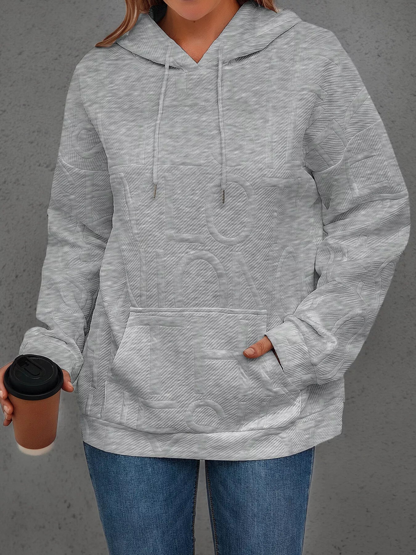 Person wearing a gray hoodie holding a coffee cup against a gray background