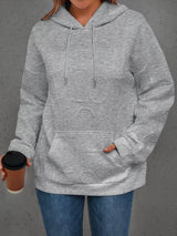 Person wearing a gray hoodie holding a coffee cup against a gray background