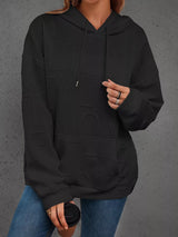 Person wearing a black hoodie with a textured pattern on a gray background
