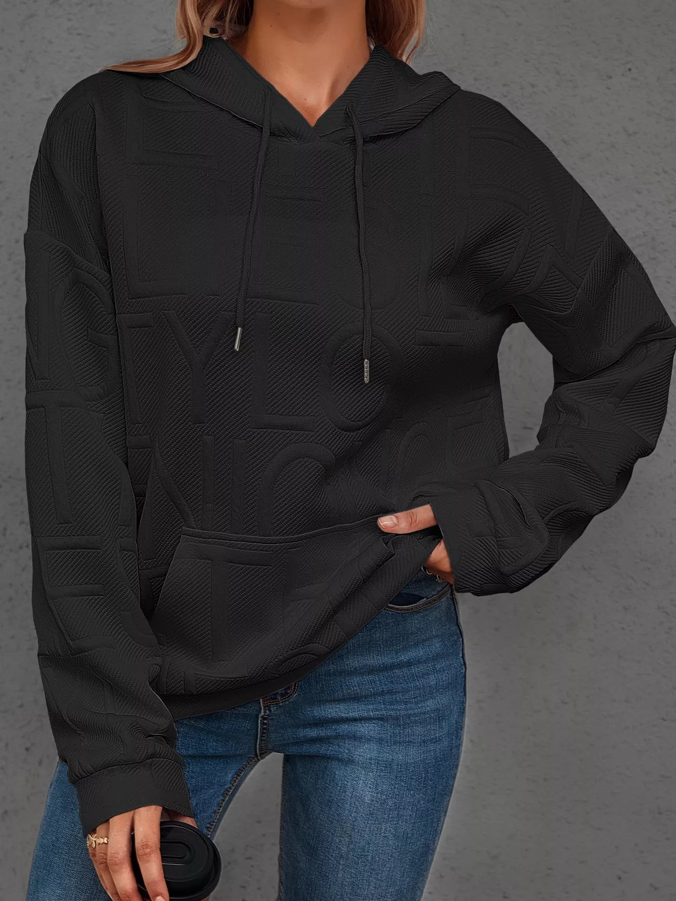 Person wearing a black hoodie and blue jeans on a gray background