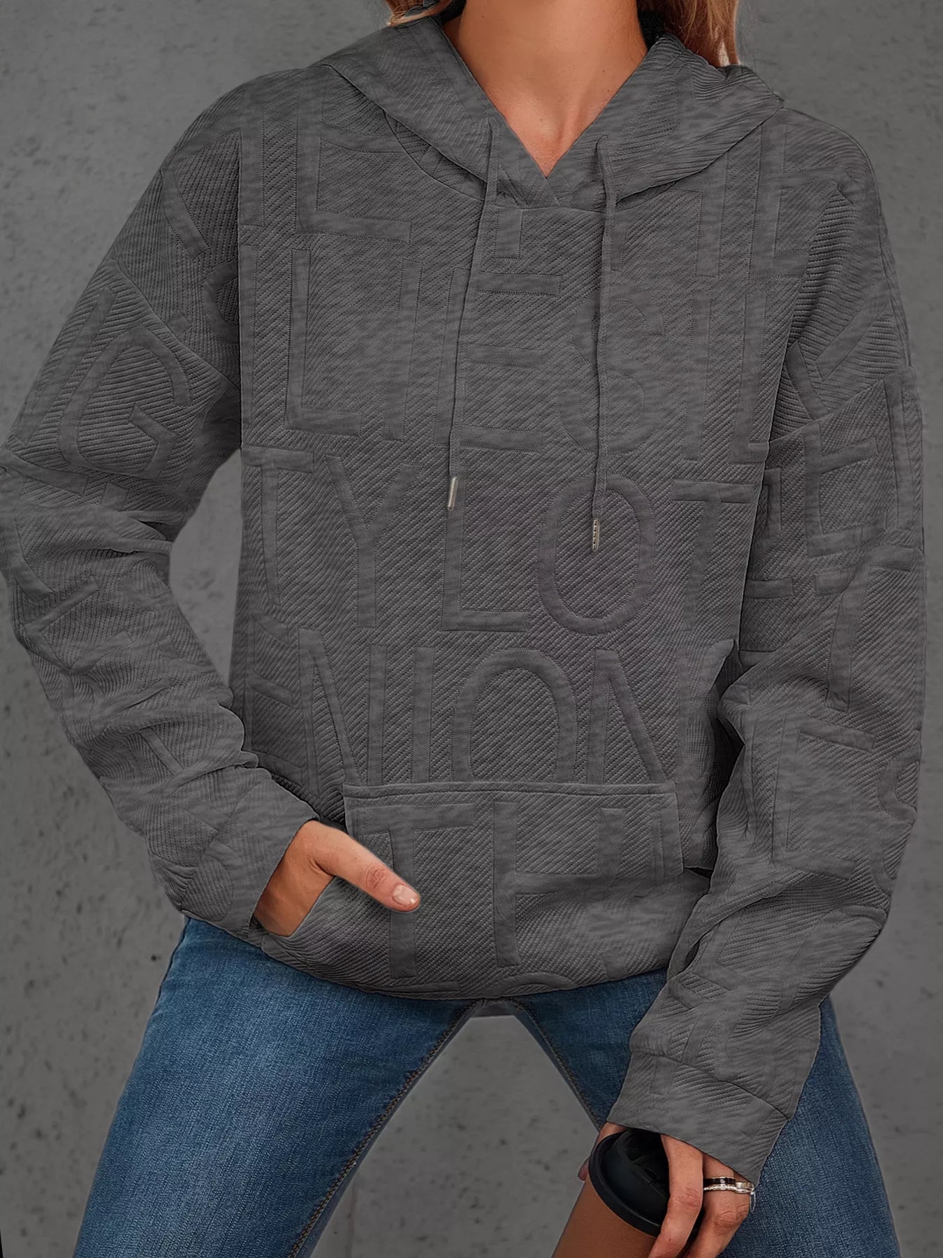 Person wearing a gray hoodie with a textured pattern on a gray background