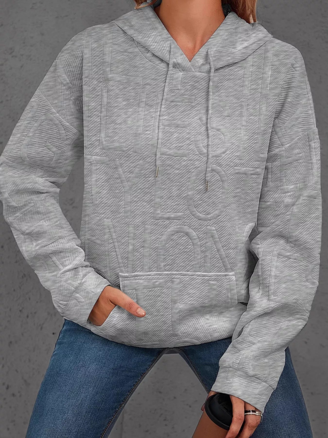 Person wearing a gray textured hoodie and blue jeans on a gray background