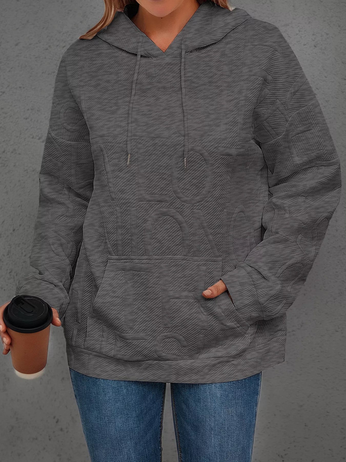 Person wearing a gray hoodie holding a coffee cup against a gray background
