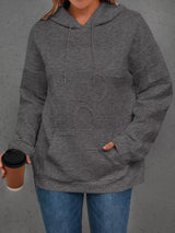 Person wearing a gray hoodie holding a coffee cup against a gray background
