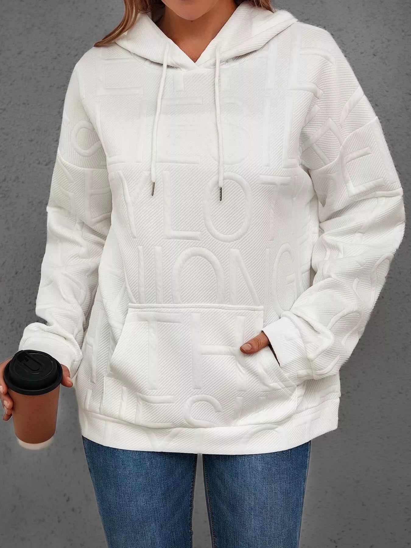 Person wearing a white hoodie with a brand logo, holding a coffee cup against a gray background