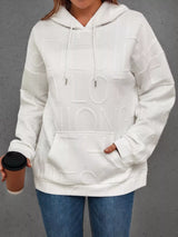 Person wearing a white hoodie with a brand logo, holding a coffee cup against a gray background