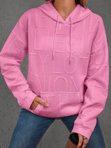 Person wearing a pink textured hoodie with text on a gray background