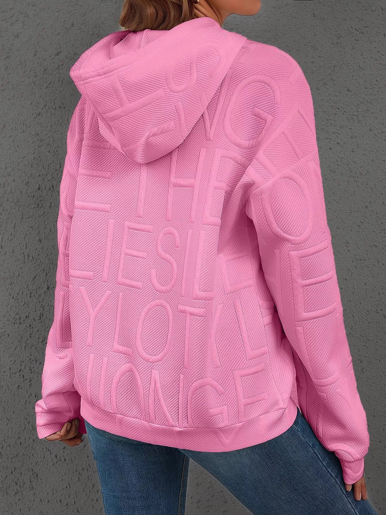 Pink hoodie with text on the back worn by a person, against a gray background