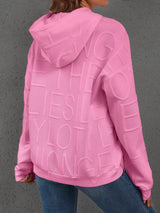 Pink hoodie with text on the back worn by a person, against a gray background