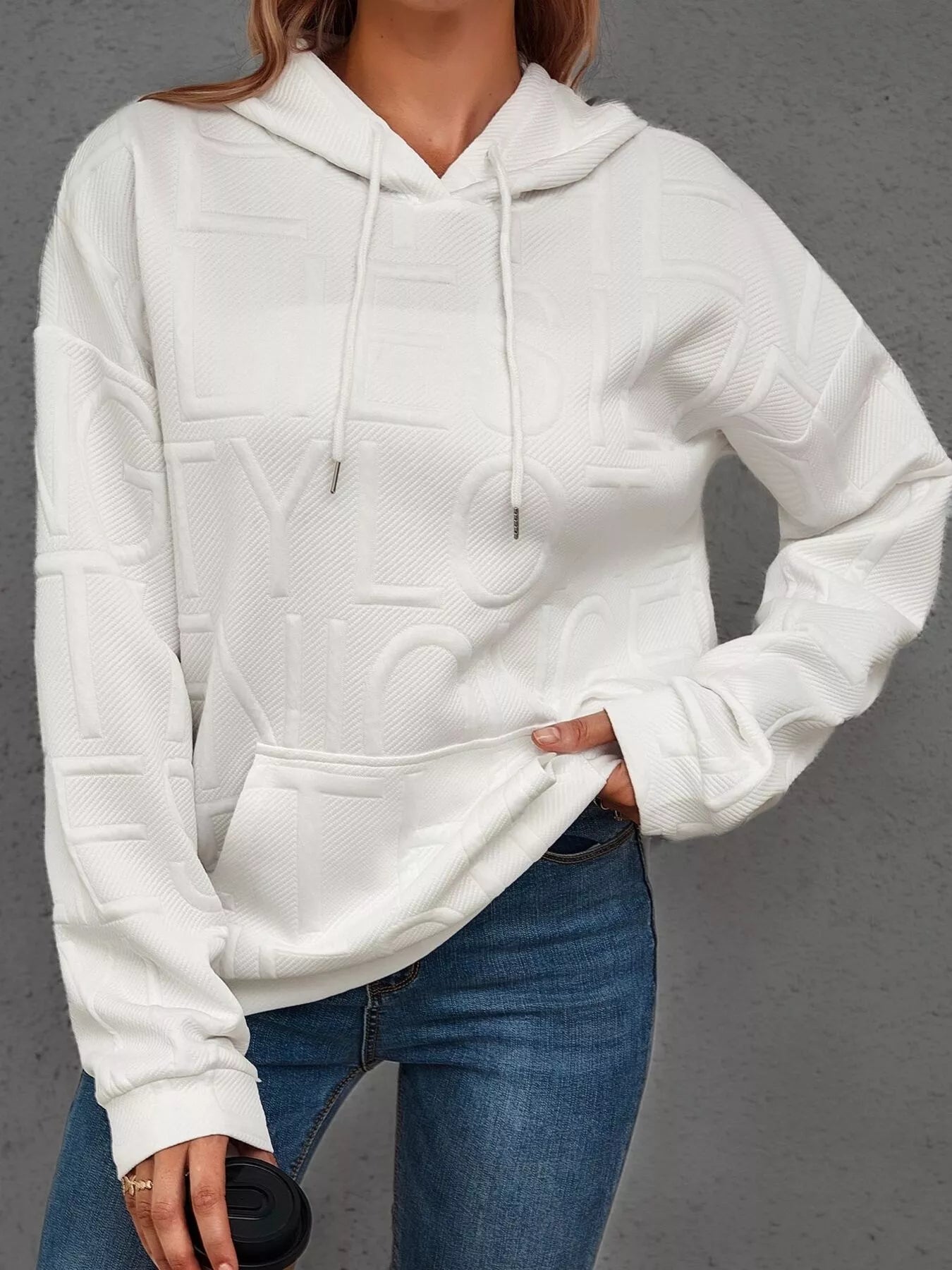 Person wearing a white hoodie and blue jeans on a gray background