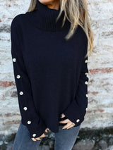 Woman wearing a black ribbed turtleneck sweater with decorative button sleeves and jeans.