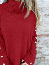 Woman wearing a burgundy ribbed turtleneck sweater with decorative button sleeves and jeans.