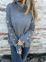 Woman wearing a dark gray ribbed turtleneck sweater with decorative button sleeves and jeans.