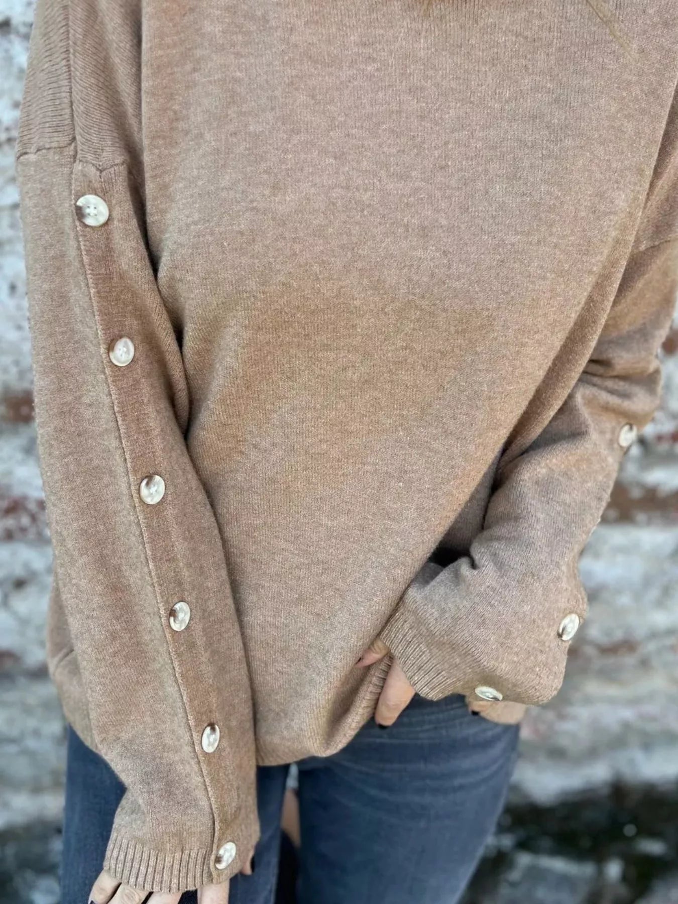 Woman wearing a khaki ribbed turtleneck sweater with decorative button sleeves and jeans.
