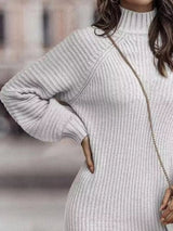 Woman wearing a white turtleneck raglan sleeve sweater dress paired with white knee-high boots and a white crossbody bag for a chic fall outfit.