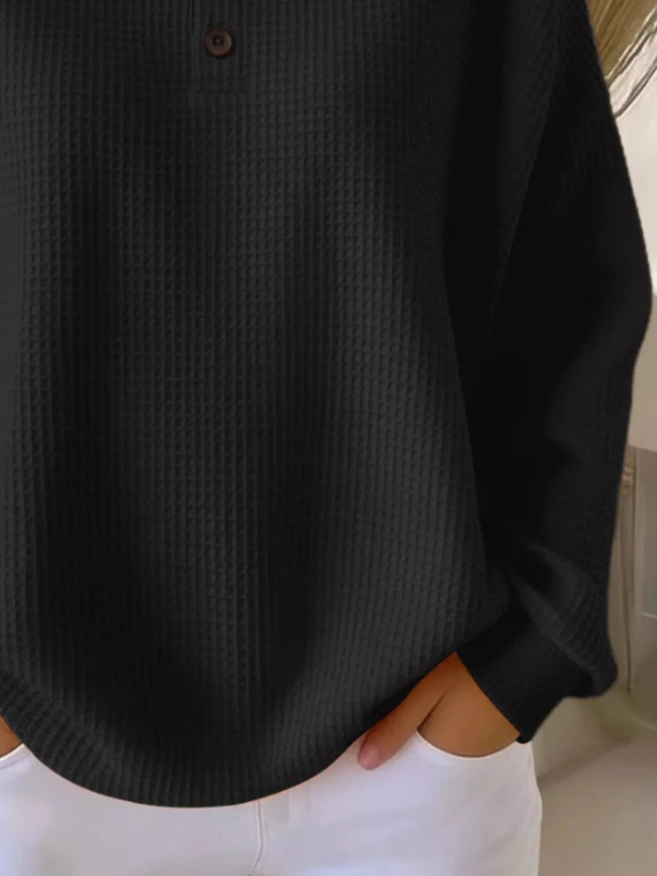 Black textured shirt worn by a person with white pants in a neutral setting