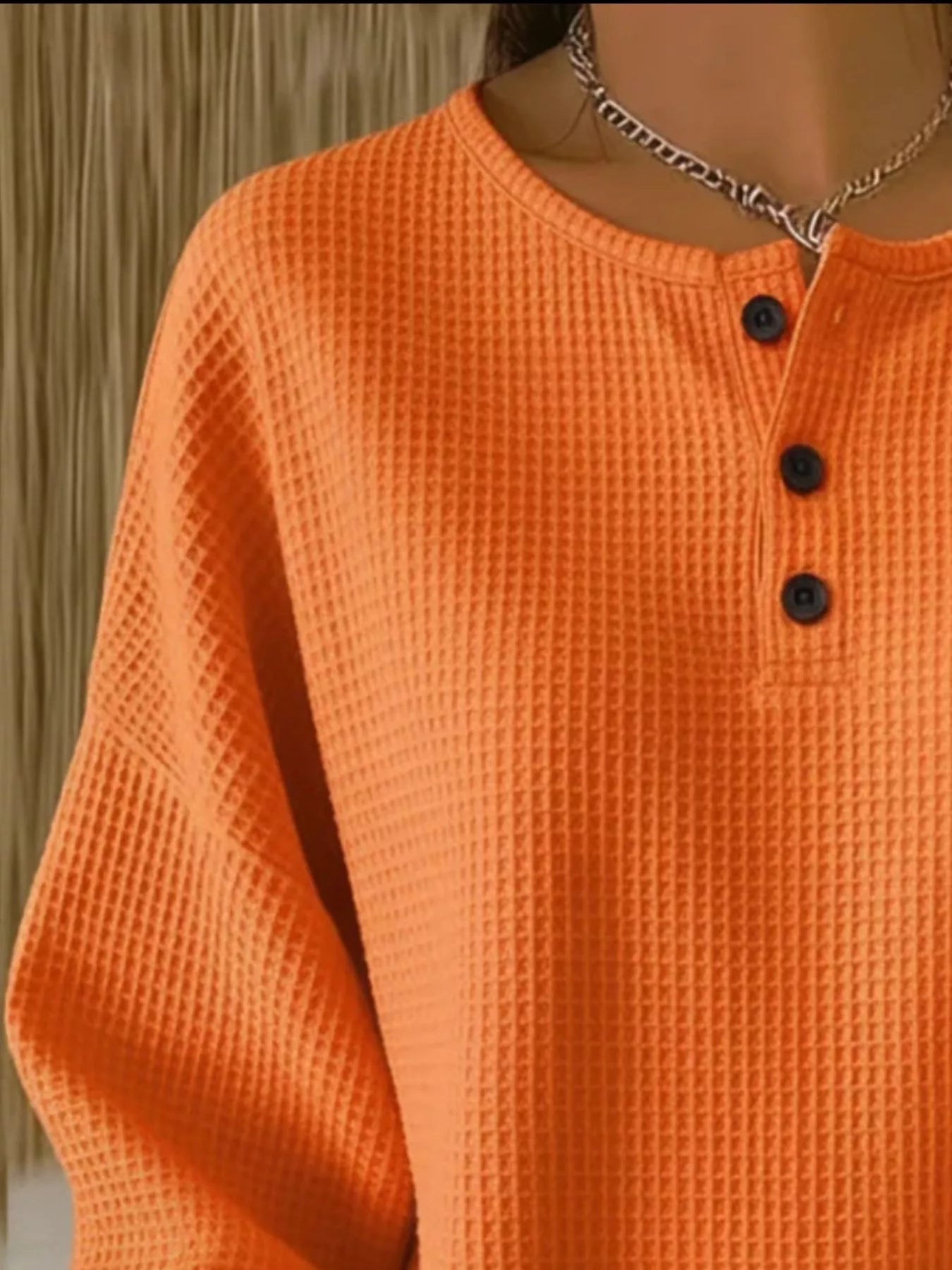 Close-up of an orange textured shirt with black buttons on a blurred background